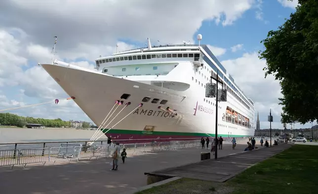 People walk past the British cruise ship Ambition, as French authorities have ordered 1,700 passengers and crew to stay on board due to a gastrointestinal illness outbreak, in Bordeaux, southwestern France, Wednesday, May 13, 2026. (AP Photo/Caroline Blumberg)