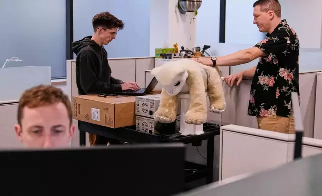 Software engineer Colin Soguero, standing at left, and creative director Morgan Pope, right, work on Familiar, an AI pet robot, prior to a demonstration at the Massachusetts-based startup Familiar Machines &amp; Magic, Wednesday, April 29, 2026, in Woburn, Mass. (AP Photo/Charles Krupa)