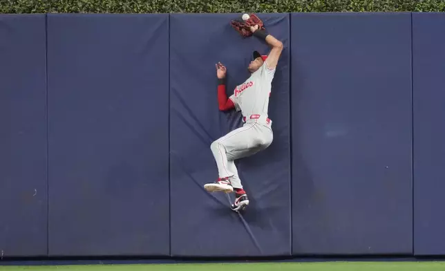 Philadelphia Phillies center fielder Justin Crawford (2) collides with the fence in center field chasing a fly ball hit by Miami Marlins shortstop Otto Lopez (6) that was later ruled a ground rule double during the first inning of a baseball game, Friday, May 1, 2026, in Miami. (AP Photo/Jim Rassol)