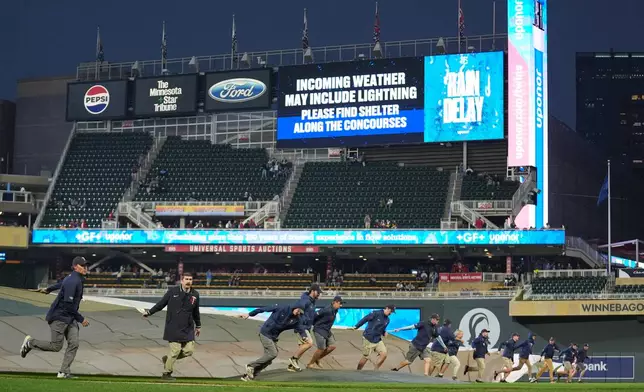 Grounds crew members place a tarp over the field during a rain delay in the fifth inning of a baseball game between the Minnesota Twins and the Houston Astros, Monday, May 18, 2026, in Minneapolis. (AP Photo/Abbie Parr)