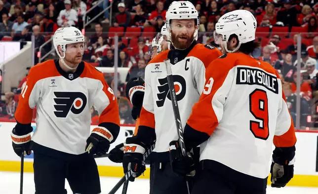 Philadelphia Flyers' Sean Couturier (14) talks with Jamie Drysdale (9) as Carl Grundstrom (91) looks on prior to a face-off during the second period of Game 2 of an NHL hockey Stanley Cup second-round playoff series against the Carolina Hurricanes in Raleigh, N.C., Monday, May 4, 2026. (AP Photo/Karl DeBlaker)