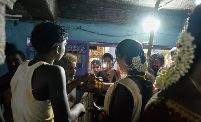 A priest ties a sacred thread on the hand of a transgender participant symbolically marrying the Hindu god Aravan during the Koovagam festival in Kallakurichi district in the southern Indian state of Tamil Nadu, Tuesday, April 28, 2026. (AP Photo/Mahesh Kumar A.)
