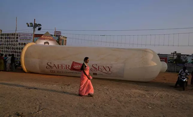 A transgender beauty pageant participant walks past a large condom replica displayed at a health awareness event during the Koovagam festival in Villupuram, Tamil Nadu, India. Sunday, April 26, 2026. (AP Photo/Mahesh Kumar A.)
