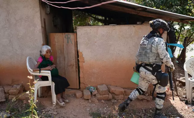 A National Guardsman walks past a resident sitting outside her home after armed attacks by local criminal groups forced more than dozens of residents to flee, in Tula, Mexico, Friday, May 15, 2026. (AP Photo/Marco Ugarte)