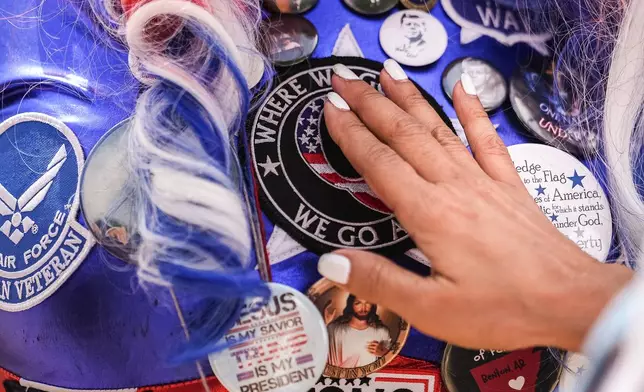 A visually impaired person feels QAnon patches on the outfit of Micki Larson-Olson, who was convicted on a misdemeanor charge for her actions on January 6, 2021, when supporters of President Donald Trump stormed the U.S. Capitol, during Rededicate 250, a mostly conservative Christian prayer gathering in honor of the United States' 250th anniversary, on the National Mall, Sunday, May 17, 2026, in Washington. (AP Photo/Julia Demaree Nikhinson)
