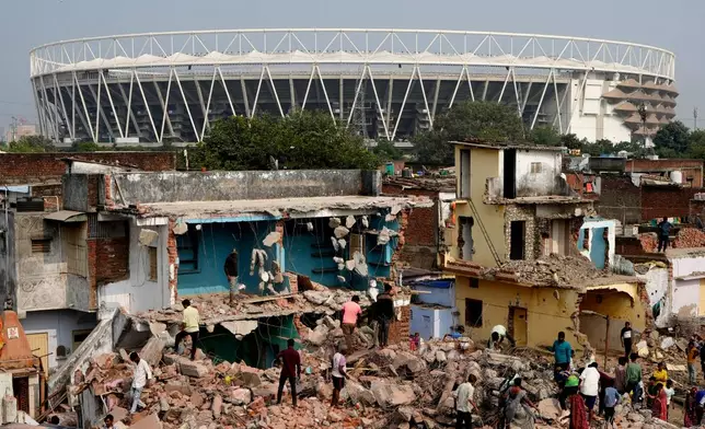 FILE - People search in the rubble after authorities demolished various structures near the Narendra Modi stadium, seen behind, as part of the preparations for the 2030 Commonwealth Games in Ahmedabad, India, Saturday, Nov. 29, 2025. (AP Photo/Ajit Solanki,File)