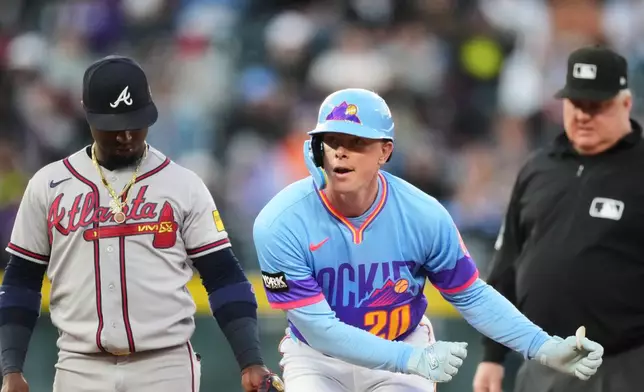 Colorado Rockies'Troy Johnston, center, gestures to the dugout after reaching second base on a double as Atlanta Braves second baseman Ozzie Albies, left, and second base umpire Bill Miller look on in the third inning of a baseball game Friday, May 1, 2026, in Denver. (AP Photo/David Zalubowski)
