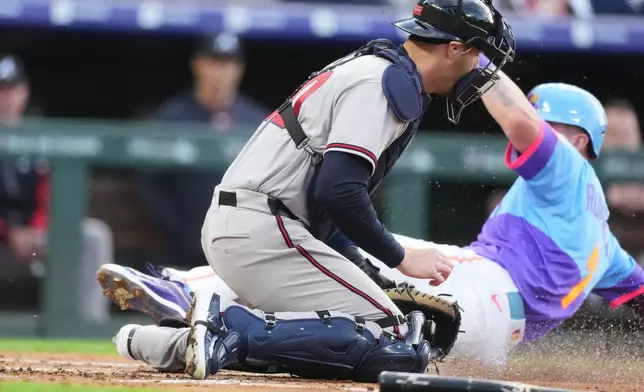 Atlanta Braves catcher Jonah Heim, front, tries to field the throw as Colorado Rockies' TJ Rumfield scores on a ground out by Willi Castro in the first inning of a baseball game Friday, May 1, 2026, in Denver. (AP Photo/David Zalubowski)