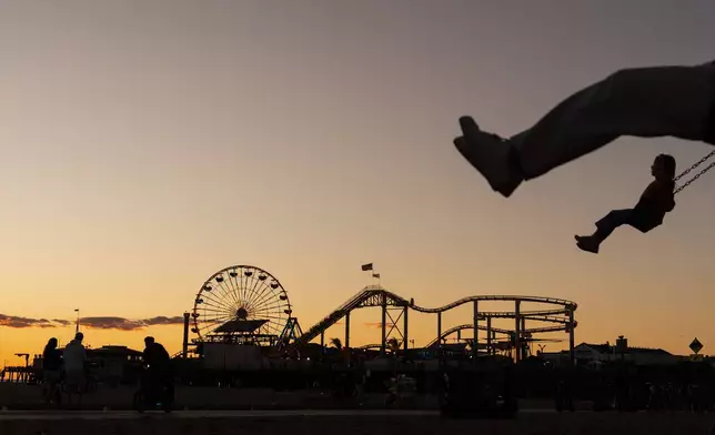 Children swing in silhouette near the Santa Monica Pier, which displays the "End of the Trail" Route 66 sign in Santa Monica, Calif., Nov. 22, 2025. (AP Photo/Jae C. Hong)