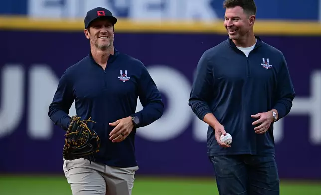 Former Cleveland Indians starting pitcher Corey Kluber, left, walks with former Indians catcher Yan Gomes before throwing out the first pitch during a reunion of the 2016 Cleveland Indians team before a baseball game against between the Cleveland Guardians and Cincinnati Reds, Friday, May 15, 2026, in Cleveland. (AP Photo/David Dermer)