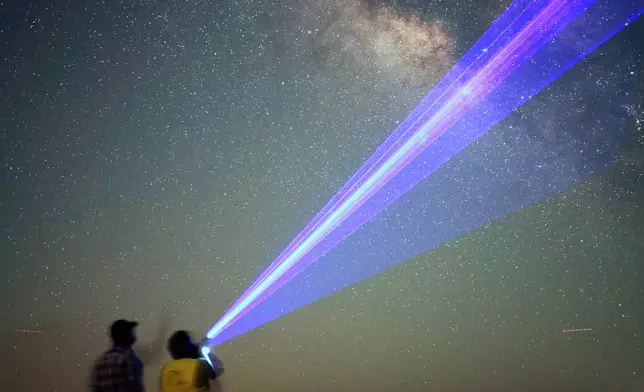 This long-exposure photograph shows men using a laser pointer to name the stars in the Milky Way galaxy in the Al Quaa Desert outside of Abu Dhabi, United Arab Emirates, Sunday, May 24, 2026. (AP Photo/Jon Gambrell)