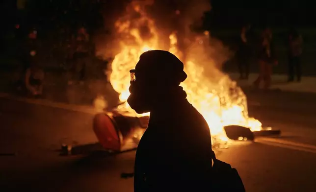 A man wearing protective gear walks in front of a burning barricade outside the Delaney Hall detention center during a protest against the transfer of detainees and federal immigration policies on Saturday, May 30, 2026, in Newark, N.J. (AP Photo/Andres Kudacki)
