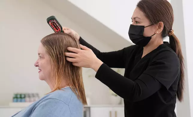Head spa specialist Ha Truong, right, uses a Red and Blue light brush on Liz Evans to help with hair growth and reduce bacteria while massaging the scalp to help the scalp serum absorb during a treatment at Sunday Headspa Thursday, April 16, 2026, in San Francisco. (AP Photo/Jeff Chiu)