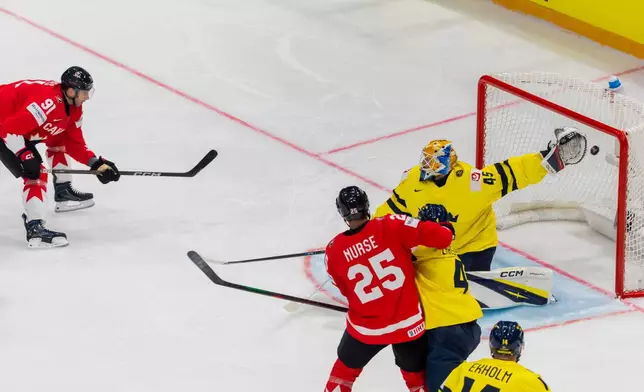 Canada's John Tavares, left, scores against Sweden goaltender Magnus Hellberg, during the 2026 IIHF Men's Ice Hockey World Championship preliminary round group B game between Canada and Sweden, at the BCF Arena ice hockey stadium, in Fribourg, Switzerland, Friday, May 15, 2026. (Salvatore Di Nolfi/Keystone via AP)