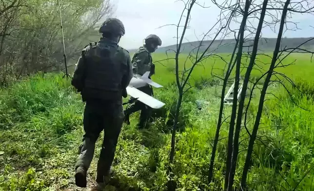 In this image made from video provided by Russian Defense Ministry Press Service on Wednesday, May 20, 2026, Russian servicemen carry an interceptor drone to launch for an action in an undisclosed location in Ukraine. (Russian Defense Ministry Press Service via AP)