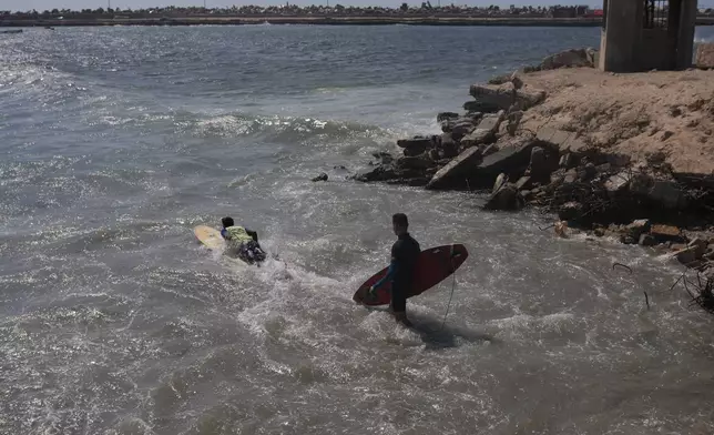 Palestinians Khalil Abu Jayyab, left, and Abed Rahim Alostaz enter the waters of the Mediterranean Sea to surf at the beach in Gaza City, Monday, May 4, 2026. (AP Photo/Jehad Alshrafi)