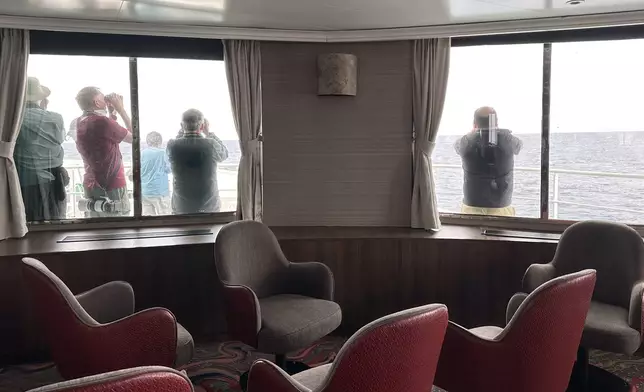 Passengers on the hantavirus-stricken cruise ship, MV Hondius, scan the horizon with binoculars during their voyage to Spain's port of Tenerife, May 6, 2026. (AP Photo)