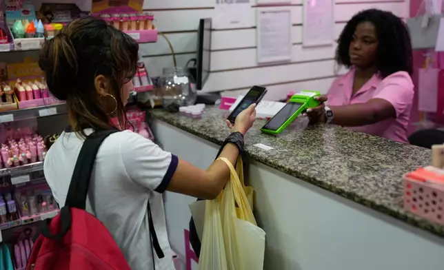 A woman pays using Pix, a free payment system, at a store in Rio de Janeiro, Thursday, April 16, 2026. (AP Photo/Silvia Izquierdo)