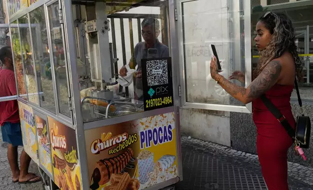A woman pays for pop corn with the Pix free payment system in Rio de Janeiro, Thursday, April 16, 2026. (AP Photo/Silvia Izquierdo)
