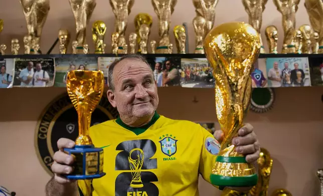 Jarbas Meneghini Carlini poses for a photo holding FIFA World Cup trophy replicas he made, at his home in Rio de Janeiro, Friday, May 15, 2026. (AP Photo/Bruna Prado)