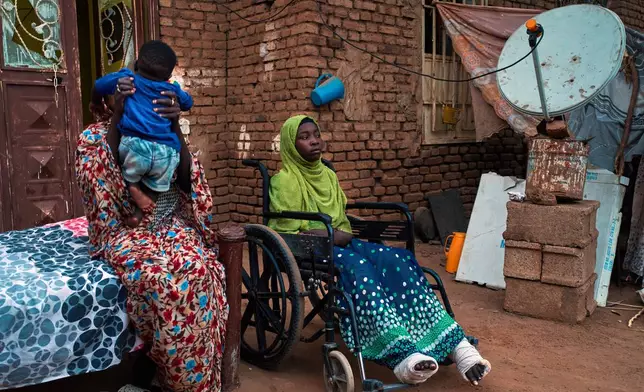 Noon Madani, 18, center, who was injured in a shelling attack, sits in a wheelchair on the patio of her family home in Khartoum, Monday, April 27, 2026. (AP Photo/Bernat Armangue)