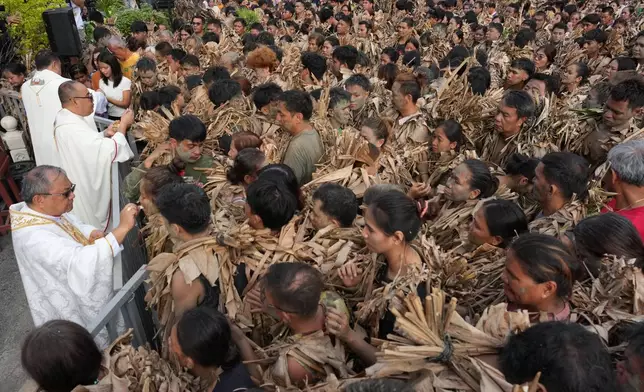 Catholic devotees covered in mud and dried banana leaves receive communion at the mud people festival on the feast day of Saint John the Baptist at Bibiclat, Nueva Ecija province, northern Philippines on Wednesday, June 24, 2026. (AP Photo/Aaron Favila)