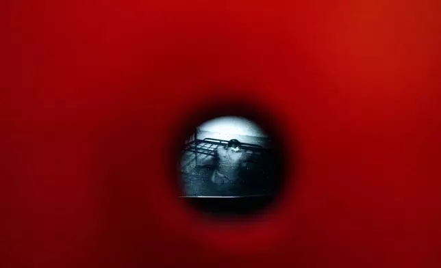 A video from the Communist era secret police surveillance archives, seen through a pinhole, shows Anton Uncu sitting on a metal bed, a day before the opening of the "A.REST 1989 — The Securitate Video Archive" exhibition, at the National History Museum of Romania, in Bucharest, Romania, Monday, June 15, 2026. (AP Photo/Andreea Alexandru)
