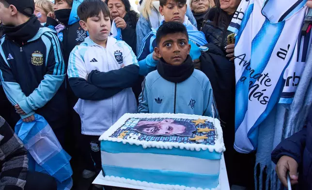 Boys stand next to a cake that reads in Spanish: "Happy Birthday", during a celebration to sing Lionel Messi happy birthday at a street mural honoring him in Buenos Aires, Argentina, Wednesday, June 24, 2026. (AP Photo/Rodrigo Abd)