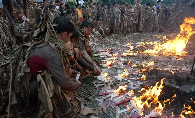 Catholic devotees covered in mud and dried banana leaves light candles as they participate at the mud people festival on the feast day of Saint John the Baptist at Bibiclat, Nueva Ecija province, northern Philippines on Wednesday, June 24, 2026. (AP Photo/Aaron Favila)