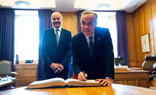 Prime Minister Mark Carney signs the Guest Book as Micheal Martin, Ireland's head of government looks on, at the Government Buildings in Dublin, on Saturday, June 13, 2026. (Christopher Katsarov /The Canadian Press via AP)