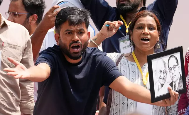 Abhijeet Dipke, center, founder of the Cockroach Janta Party gestures as he holds the photograph of Mahatma Gandhi and Bhim Rao Ambedkar during a protest demanding the resignation of Education Minister Dharmendra Pradhan over alleged examination irregularities and repeated paper leaks in New Delhi, India, Saturday, June 20, 2026. (AP Photo/Manish Swarup)