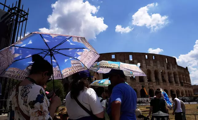 FILE - Tourists use umbrellas to shelter from the heat as they line up for a tour of the Forum in Rome, on Tuesday, July 22, 2025. (AP Photo/Gregorio Borgia, File)