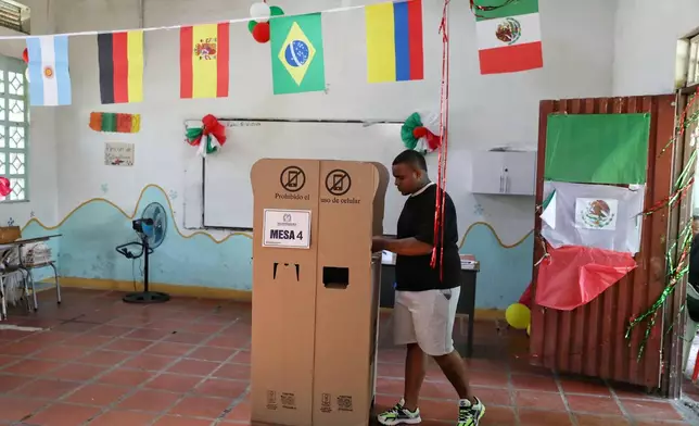 A voter marks his ballot in a classroom decorated with flags of countries participating in the World Cup serving as a polling station during the presidential runoff election in Santander de Quilichao, Colombia, Sunday, June 21, 2026. (AP Photo/Santiago Saldarriaga)