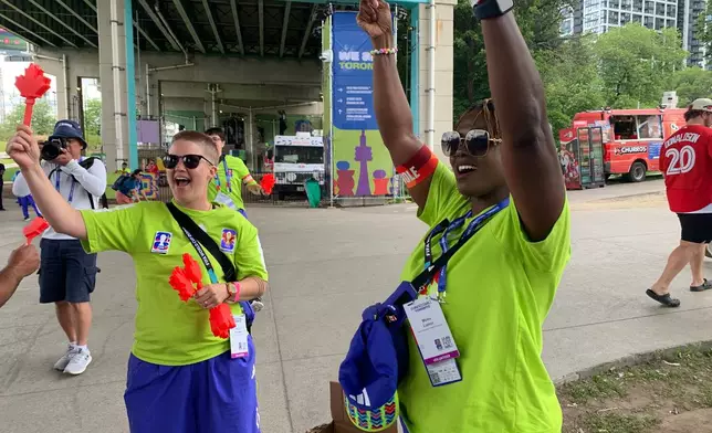 Volunteers Nicole Johnston, left, and Mbalu Lumor, right, wave "Canadian clappers" before handing them out to attendees at the FIFA Fan Festival Wednesday, June 24, 2026, in Toronto. (AP Photo/Mike Householder)