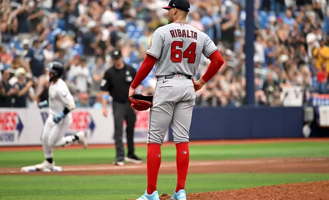 Washington Nationals pitcher Orlando Ribalta (64) looks away as Tampa Bay Rays' Jonny DeLuca, back left, rounds the bases after hitting a two-run home run during the seventh inning of a baseball game Sunday, June 21, 2026, in St. Petersburg, Fla. (AP Photo/Jason Behnken)