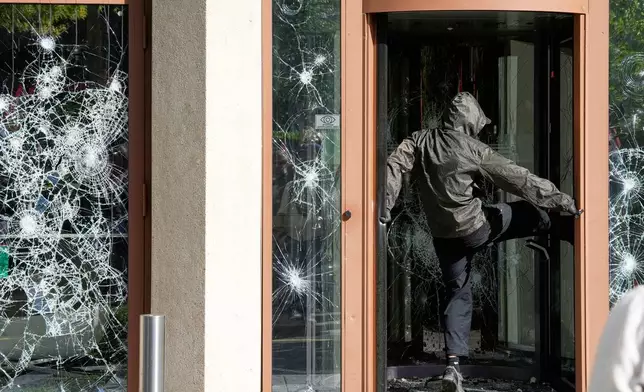 A protester kicks at a window during a "No G7" demonstration in Geneva, Switzerland, Sunday, June 14, 2026, ahead of the G7 summit scheduled to take place June 15-17. (AP Photo/Baz Ratner)