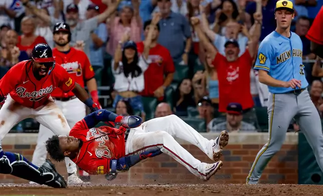 Atlanta Braves second baseman Ozzie Albies, center, scores a run as Milwaukee Brewers pitcher Jacob Misiorowski, right, and Braves' Jorge Mateo, left, look on during the sixth inning of a baseball game, Friday, June 19, 2026, in Atlanta. (AP Photo/Erik S. Lesser)