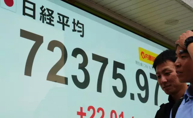 People walk past a monitor showing Japan's Nikkei 225 index at a securities firm in Tokyo, Tuesday, June 23, 2026. (AP Photo/Hiro Komae)