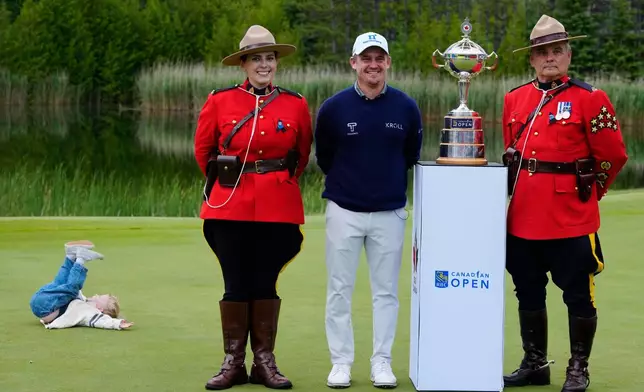 A child, left, of Bud Cauley, second from right, plays as Bud stands with two RCMP officers next to the trophy after he won the Canadian Open golf tournament in Caledon, Ontario, Sunday June 14, 2026. (Frank Gunn/The Canadian Press via AP)