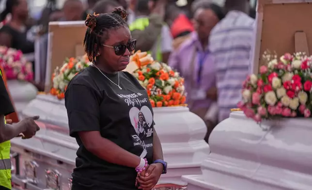 A relative grieves while standing between caskets carrying the remains of girls who died in the Utumishi Academy school fire during a memorial service at Gilgil Stadium, Nakuru County, Kenya, Friday, June 12, 2026. (AP Photo/Brian Inganga)