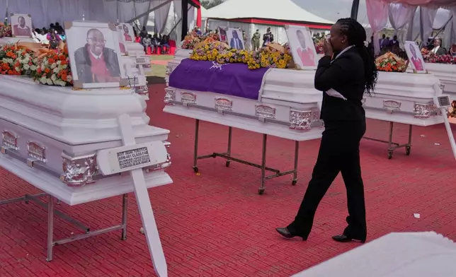 A mourner reacts as she stands between caskets carrying the remains of the 16 girls who died in the Utumishi Academy school fire during a memorial service at Gilgil Stadium, Nakuru County, Kenya, Friday, June 12, 2026. (AP Photo/Brian Inganga)