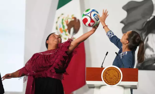 Mexican President Claudia Sheinbaum, right, and amateur soccer player Yolett Cervantes reach to catch a soccer ball during a ceremony distributing tickets to the opening match of the 2026 FIFA World Cup, at the president's daily news conference at the National Palace in Mexico City, Friday, May 29, 2026. (AP Photo/Fernando Llano)