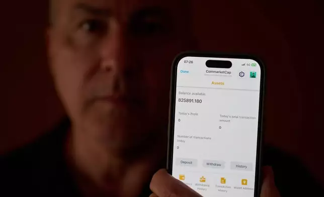 Chris Colocousis holds up a screenshot of the fake app where he invested his savings showing his account had more than doubled to nearly $826,000 as part of a scam in which he says he lost $400,000 at his home in Raynham, Mass., Tuesday, March 10, 2026. (AP Photo/David Goldman)