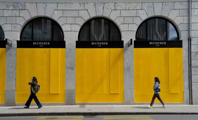 Pedestrians walk past the boarded-up windows of a shop, ahead of expected protests for the G7 summit, in Geneva, Switzerland, Tuesday, June 9, 2026. (AP Photo/Baz Ratner)