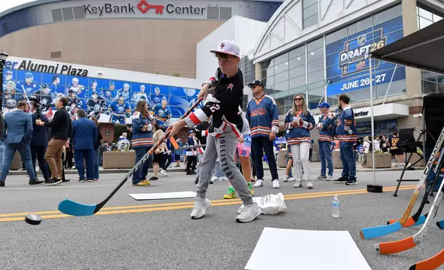 Eleven-year-old Pierce Switzer, center, shoots pucks outside Key Bank Center before the NHL hockey draft Friday, June 26, 2026, in Buffalo, N.Y. (AP Photo/Adrian Kraus)