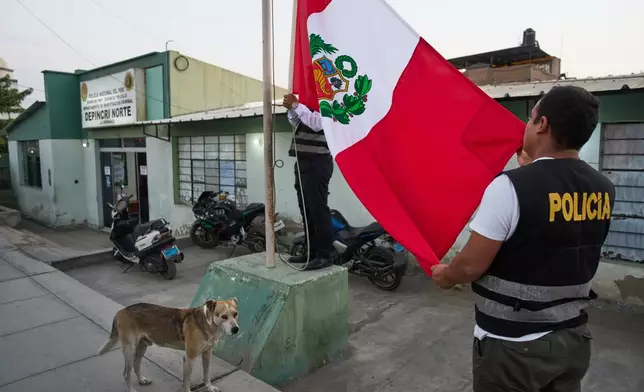 Police officers raise the Peruvian flag outside a criminal investigations unit in Trujillo, Peru, Monday, May 25, 2026. (AP Photo/Rodrigo Abd)