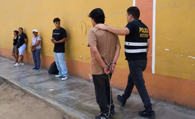 A police officer escorts a detainee accused of being part of a criminal gang after a news conference at a downtown police station in Trujillo, Peru, Thursday, May 21, 2026. (AP Photo/Rodrigo Abd)