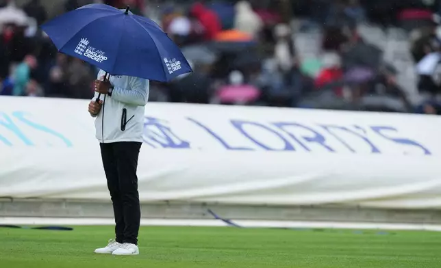 An umpire stands on the field under an umbrella as it rains during the third day of the Test match between England and New Zealand at Lord's cricket ground in London, Saturday, June 6, 2026. (AP Photo/Kirsty Wigglesworth)