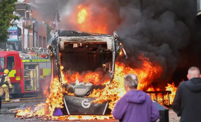 People watch as firemen arrive to put out vehicle that was set alight during a protest in East Belfast following a stabbing incident in Belfast, Tuesday, June 9, 2026. (AP Photo/Peter Morrison)