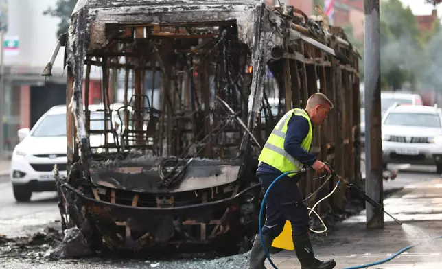 A worker clear up the debris in front of a burnt out bus, after rioting broke out late Tuesday, in east Belfast, Northern Ireland, Wednesday, June 10, 2026, following a stabbing incident. (AP Photo/Peter Morrison)